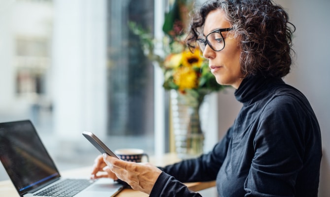 Femme regardant un téléphone portable devant un ordinateur portable